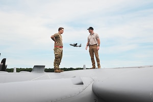 A man in uniform stands with a civilian on top of an aircraft.