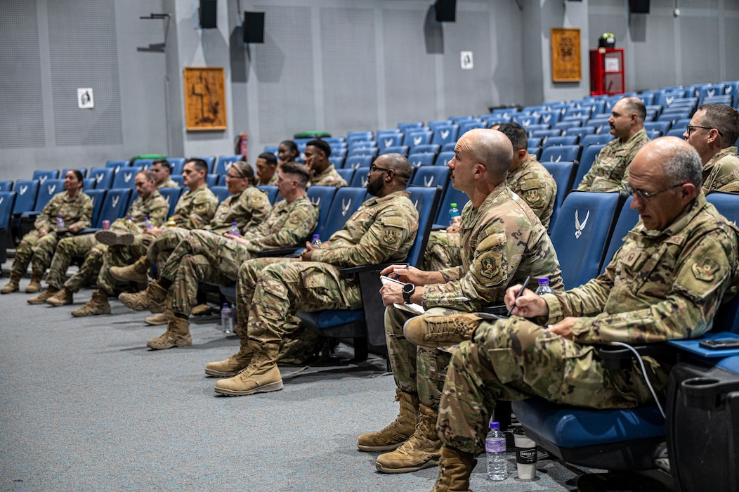 A crowd of Airmen who wish to become additional duty first sergeants fill the seats across the frame as they listen attentively to orators out of left frame