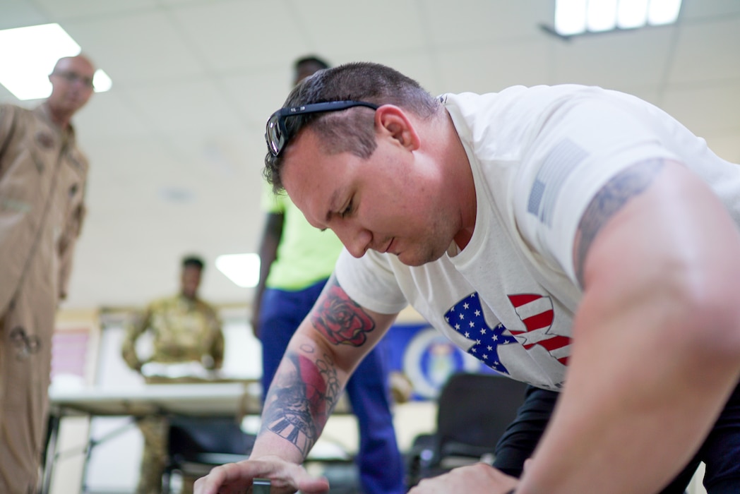 Tech. Sgt. Campanella is in the foreground, taking up most of frame as he practices assembling a litter out of frame with medical personnel behind him ready for guidance
