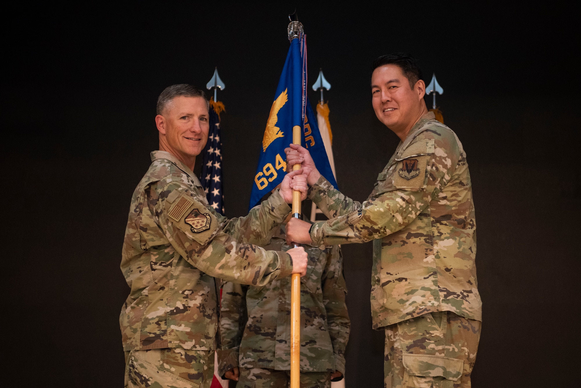 U.S. Air Force Maj. Albert Yin, right, incoming 694th Intelligence Support Squadron commander, accepts command from Col. Douglas Mabry, 694th Intelligence, Surveillance, and Reconnaissance Group commander, during the 694th ISS change of command ceremony at Osan Air Base, Republic of Korea, July 8, 2025.