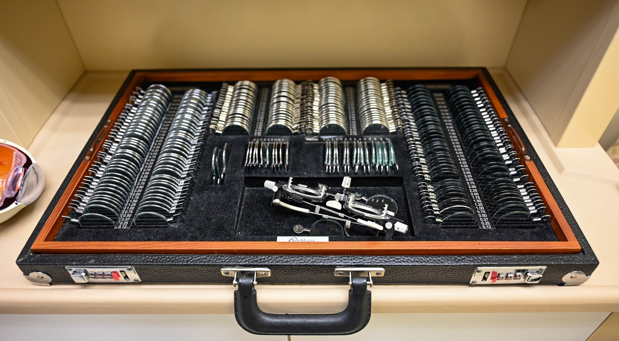 A black and brown wooden case with trial eye glass lenses sits on a shelf.