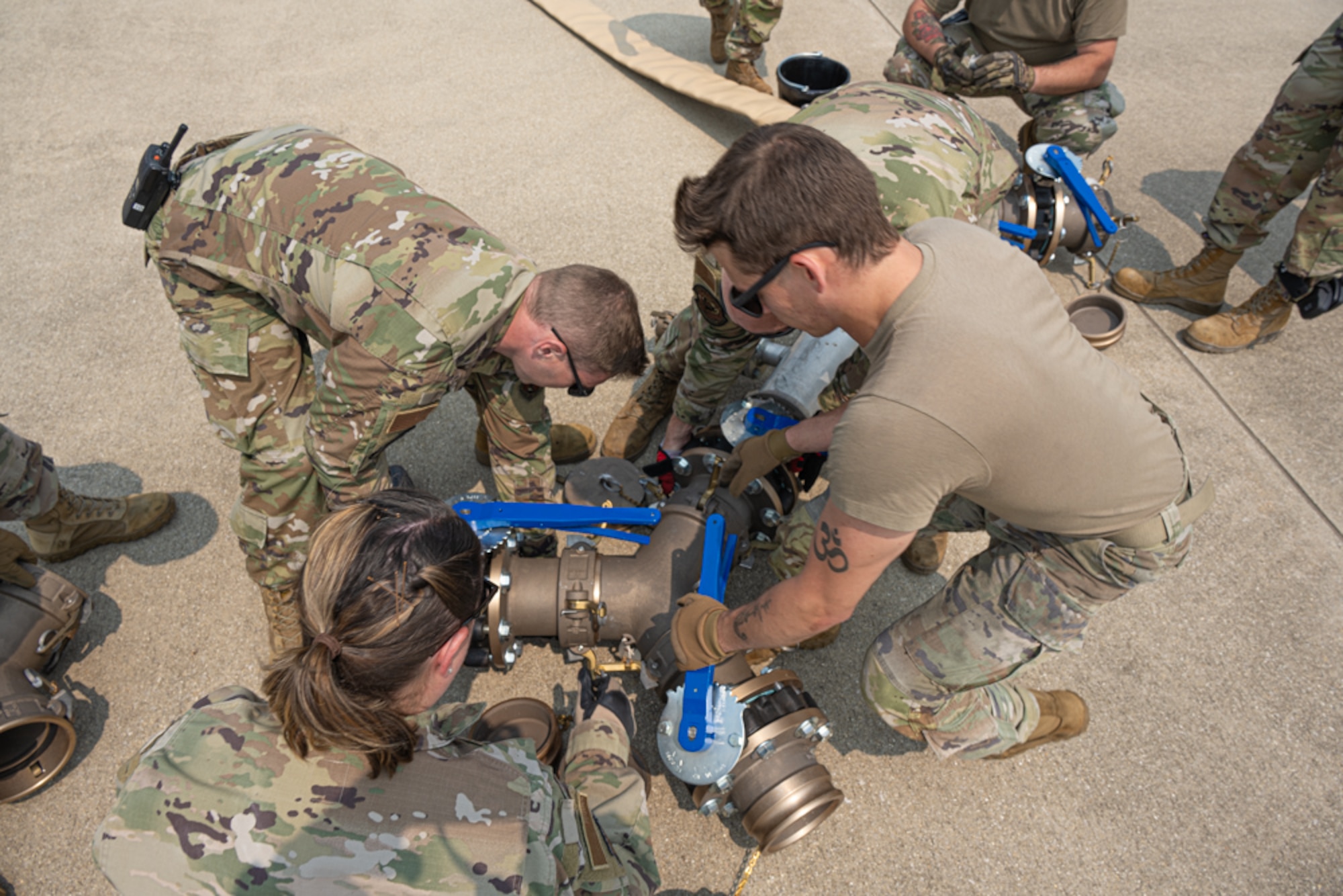 Airman work to attach a large blue "Y" connector to a hose during