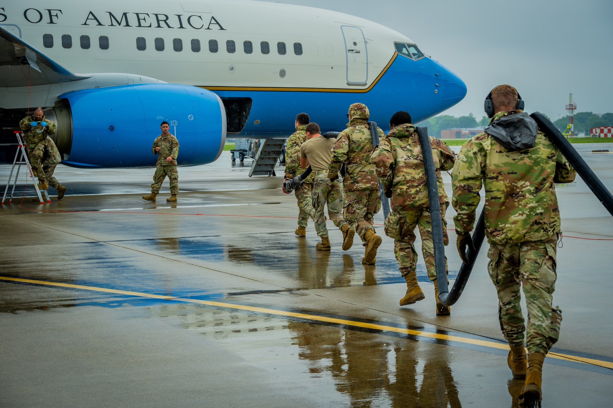 Airmen carry a hose over their shoulders out to a blue and white C-40 plane.