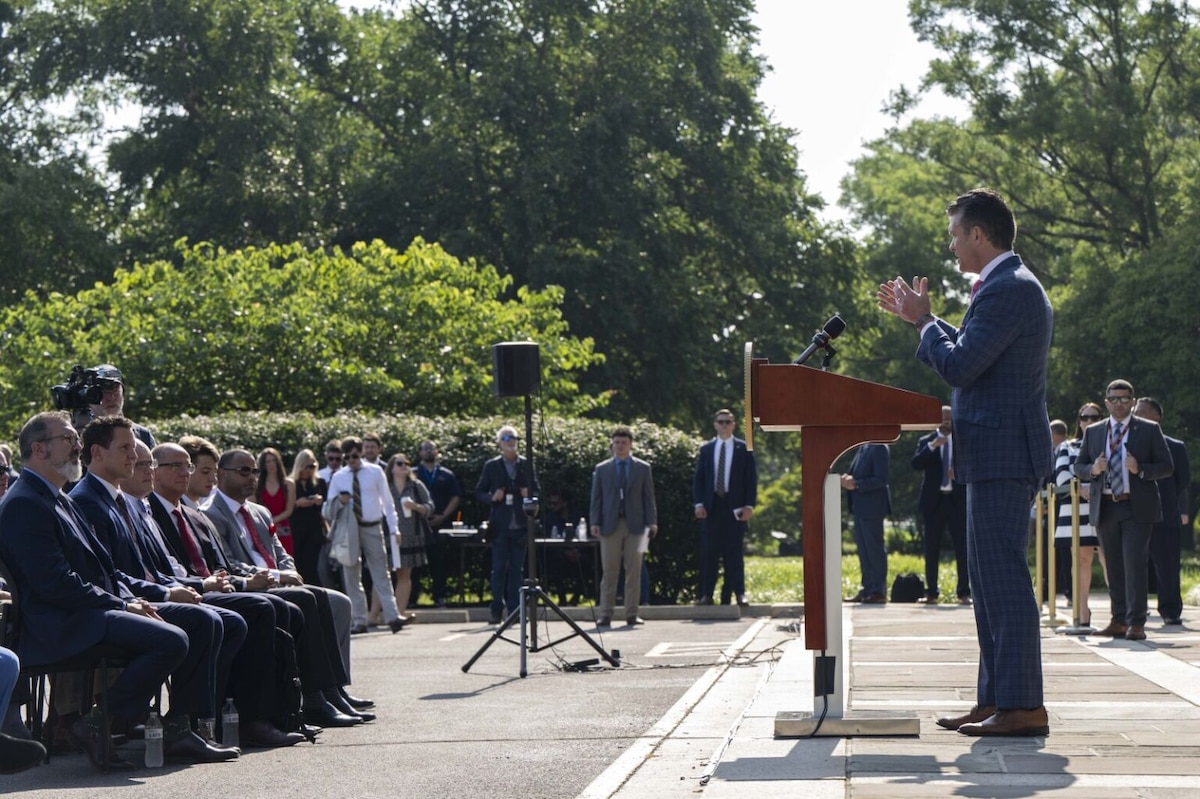 A man in business attire stands before a seated group of people and speaks at a podium.