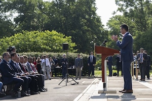 A man in business attire stands before a seated group of people and speaks at a podium.