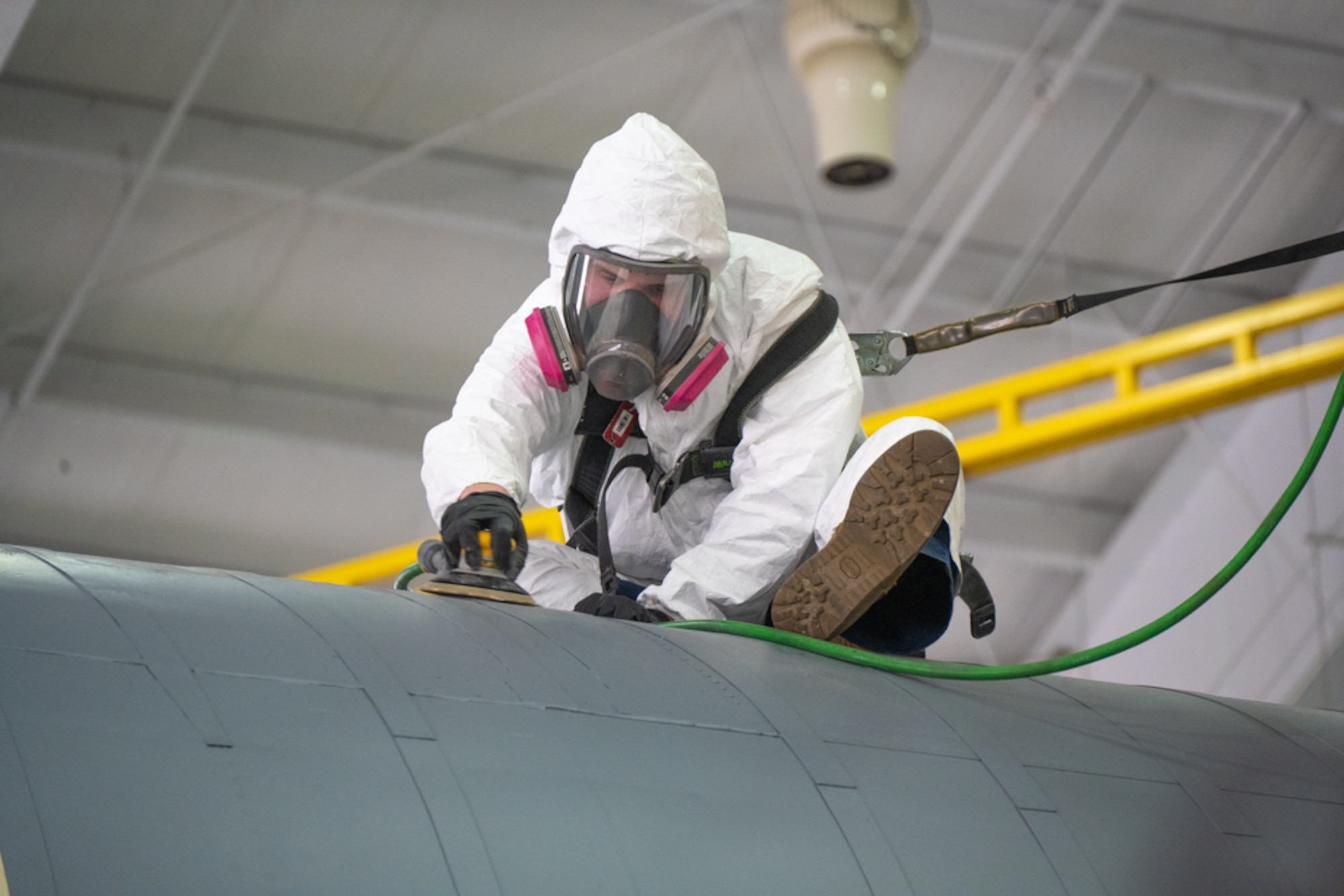 An Airman sits on top of a KC-135 Stratotanker fuselage while using a sander to sand down the jet.