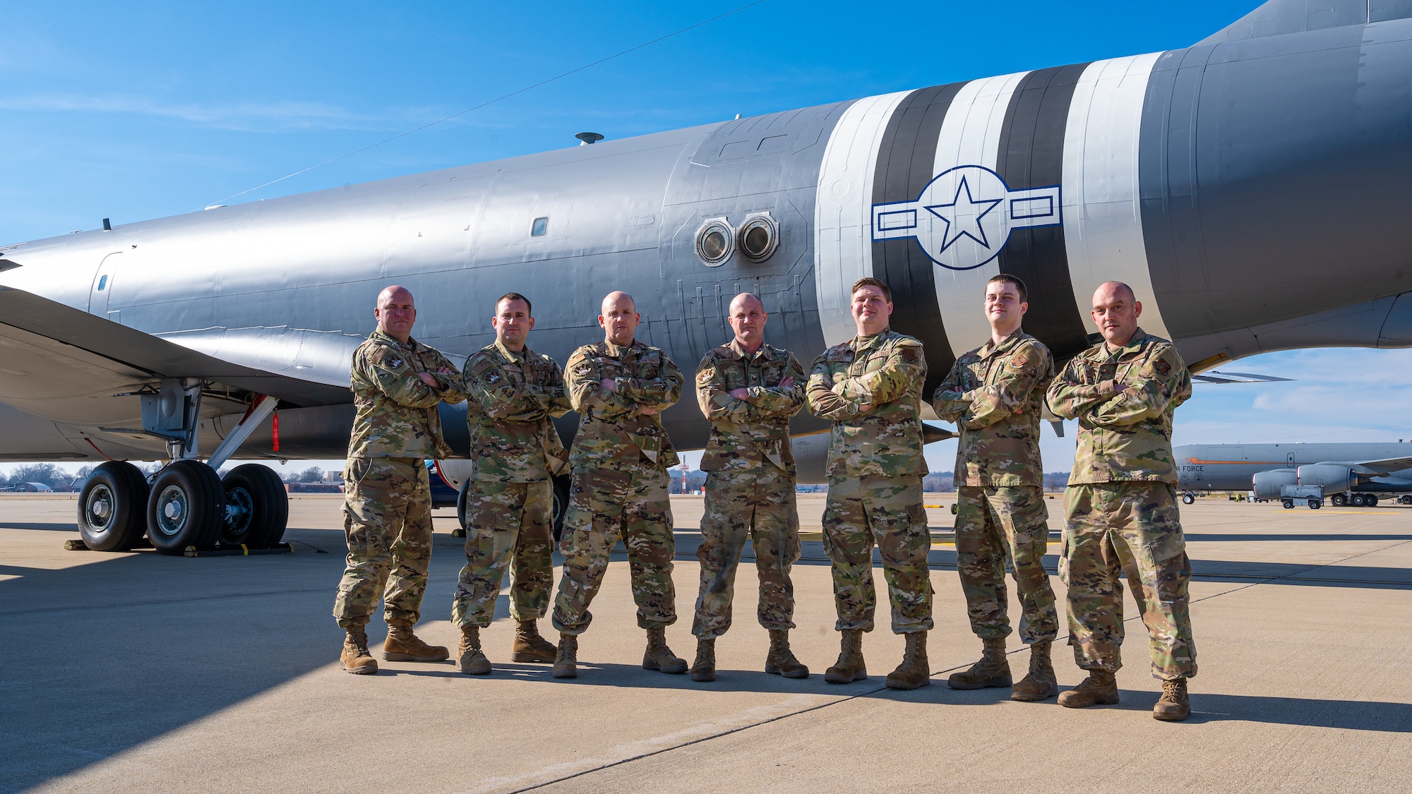 Seven Airmen stand in front of a KC-135 Stratotanker painted with D-Day invasion colors