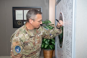 U.S. Space Force Brig. Gen. Nathan Yates, mobilization assistant to the Deputy Chief of Space Operations for Operations, Cyber, and Nuclear, signs the National Space Defense Center heritage board during a visit to the organization at Schriever Space Force Base, Colo., June 26, 2025. The purpose of the visit was to evaluate and enhance the integration of Multi-National Force partners within the NSDC’s mission set. Through the NSDC’s operational capabilities, U.S. Space Forces—Space and the Combined Joint Force Space Component maintain and protect vital global space domain capabilities against emerging adversary counterspace systems. This collaborative effort, extended through a network of Allies, partners, and commercial industry, provides a critical strategic advantage. (U.S. Space Force photo by Dalton Prejeant)