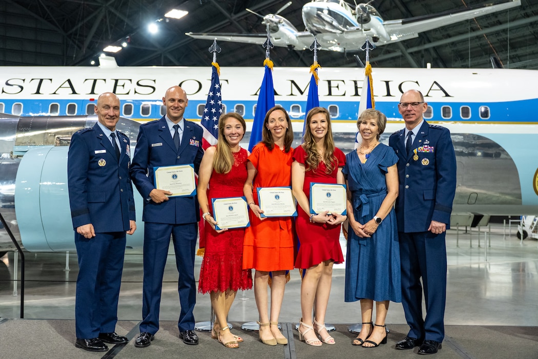 A group photo including three gentlemen in service dress uniforms, and four women, three in red dresses and one in blue
