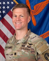 Army lieutenant colonel posing for a portrait photo in combat uniform in front of the US flag and Army Aviation flag.