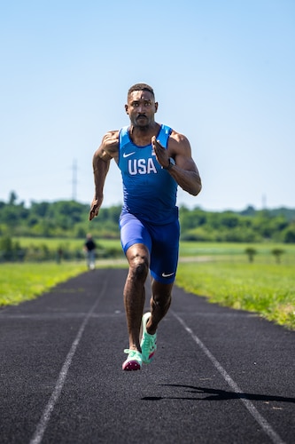 Capt. Banks sprints towards the viewer wearing a blue track outfit with USA on the chest