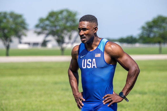 Capt. Banks stands with his hands on his hips wearing a blue track tank top with USA on the chest