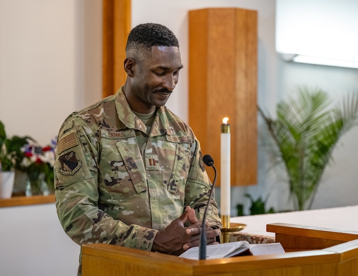 An Air Force service member, wearing camouflage uniform, stands behind a podium with a bible