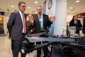 Two men in suits speak while looking at drone technology.