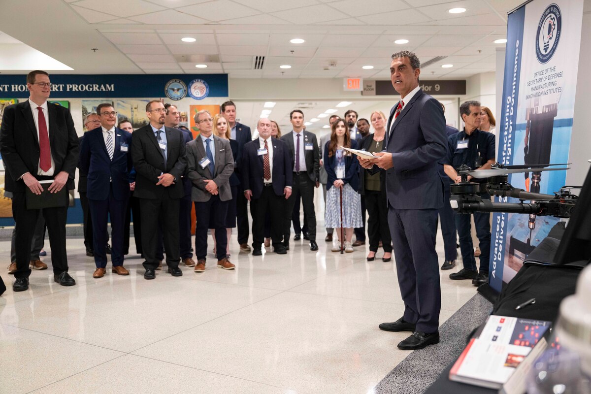 A man in a suit speaks to people in business attire inside a building filled with displays.
