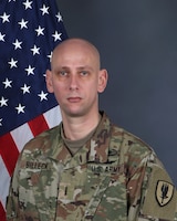 Army chief warrant officer 4 posing for a portrait photo wearing combat uniform with a US flag in the background.