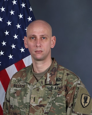 Army chief warrant officer 4 posing for a portrait photo wearing combat uniform with a US flag in the background.