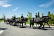 Army Soldiers wearing dark ceremonial uniforms are riding on caisson horses as the caisson is carrying a flag-draped casket down a road in Arlington National Cemetery.