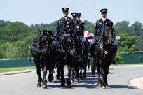 Army Soldiers are riding on caisson horses as the caisson is carrying a flag-draped casket down a road in Arlington National Cemetery.