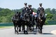 Army Soldiers are riding on caisson horses as the caisson is carrying a flag-draped casket down a road in Arlington National Cemetery.