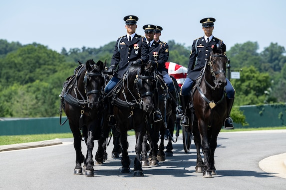 Army Soldiers are riding on caisson horses as the caisson is carrying a flag-draped casket down a road in Arlington National Cemetery.