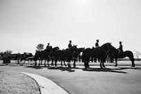Black and white image of Army Soldiers riding on caisson horses.