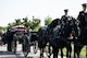 Army Soldiers from The Old Guard wearing dark ceremonial uniforms are moving a flag-draped casket from a horse-drawn caisson at Arlington National Cemetery.