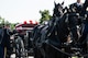 Soldiers wearing dark ceremonial uniforms are adjusting the flag that is covering a casket which is being carried on a horse-drawn caisson.