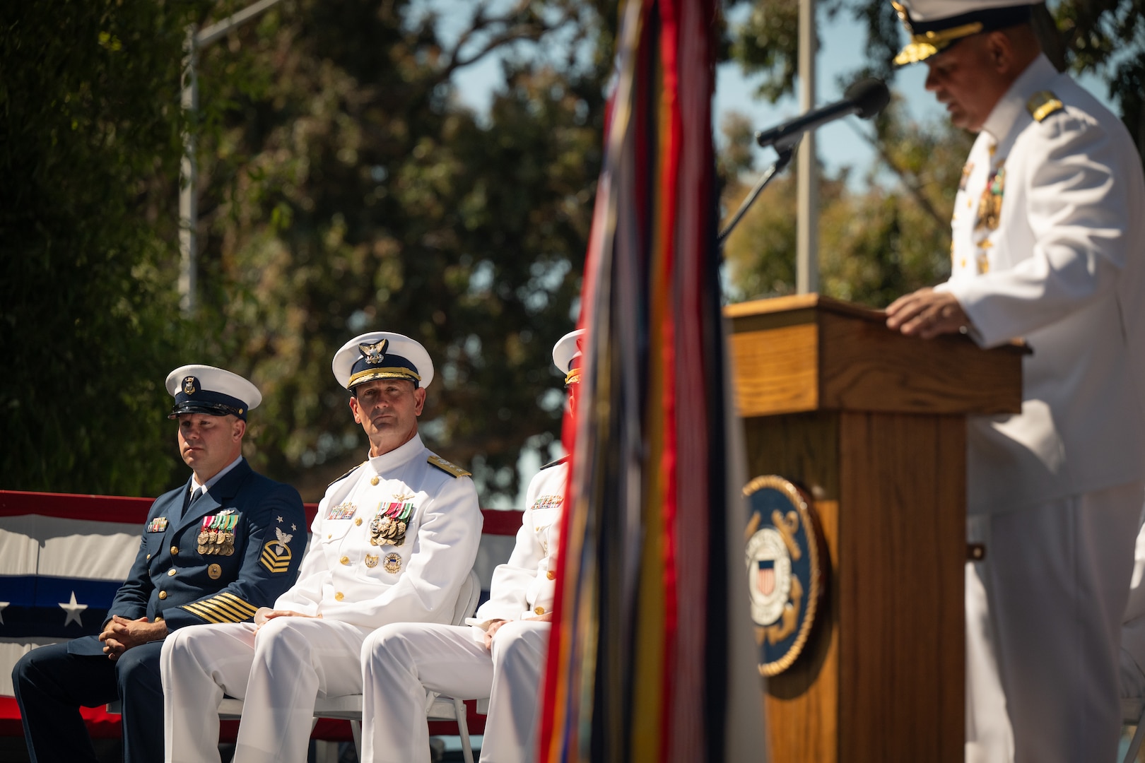 U.S. Coast Guard Rear Adm. Joseph Buzzella and Southwest District Command Master Chief Josh McBride listen to Pacific Area Commander Vice Adm. Andrew Tiongson deliver a speech during a change-of-command ceremony in Alameda, Calif., July 8, 2025.
