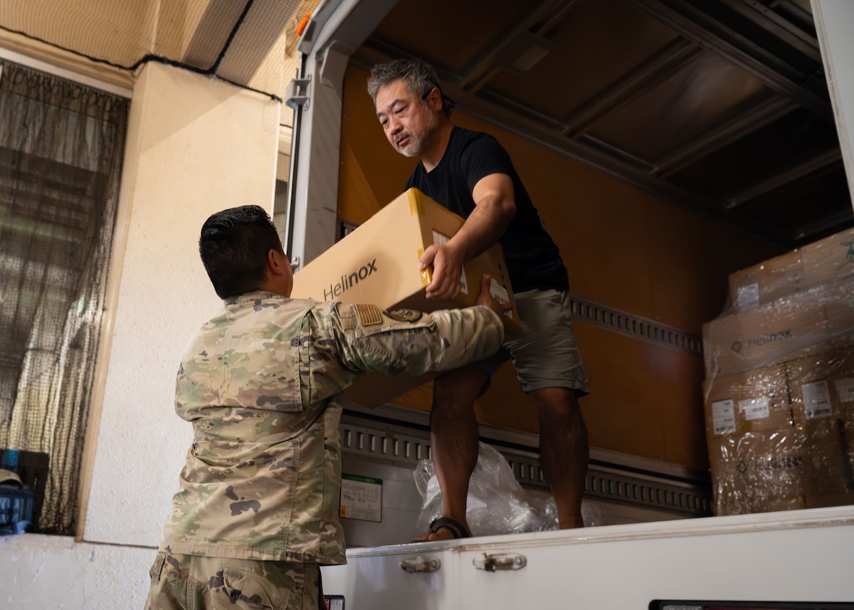 A U.S. Air Force member and a Japanese contractor unload boxes from a truck.