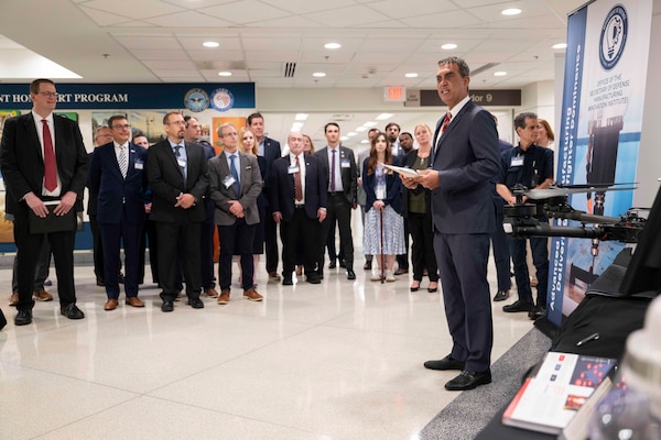A man in a suit speaks to people in business attire inside a building filled with displays.