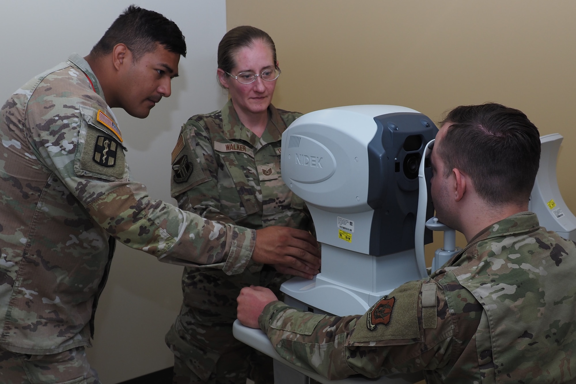 Sgt. Eduardo Morales, left, the assistant NCO in charge of the EACH Optometry Clinic, trains Air Force Tech. Sgt. Crystal Walker, and Air Force Staff Sgt. Devllin Clevenger on proper use of an auto refractor, which is used to test eye pressure and detect eye prescriptions for patients.