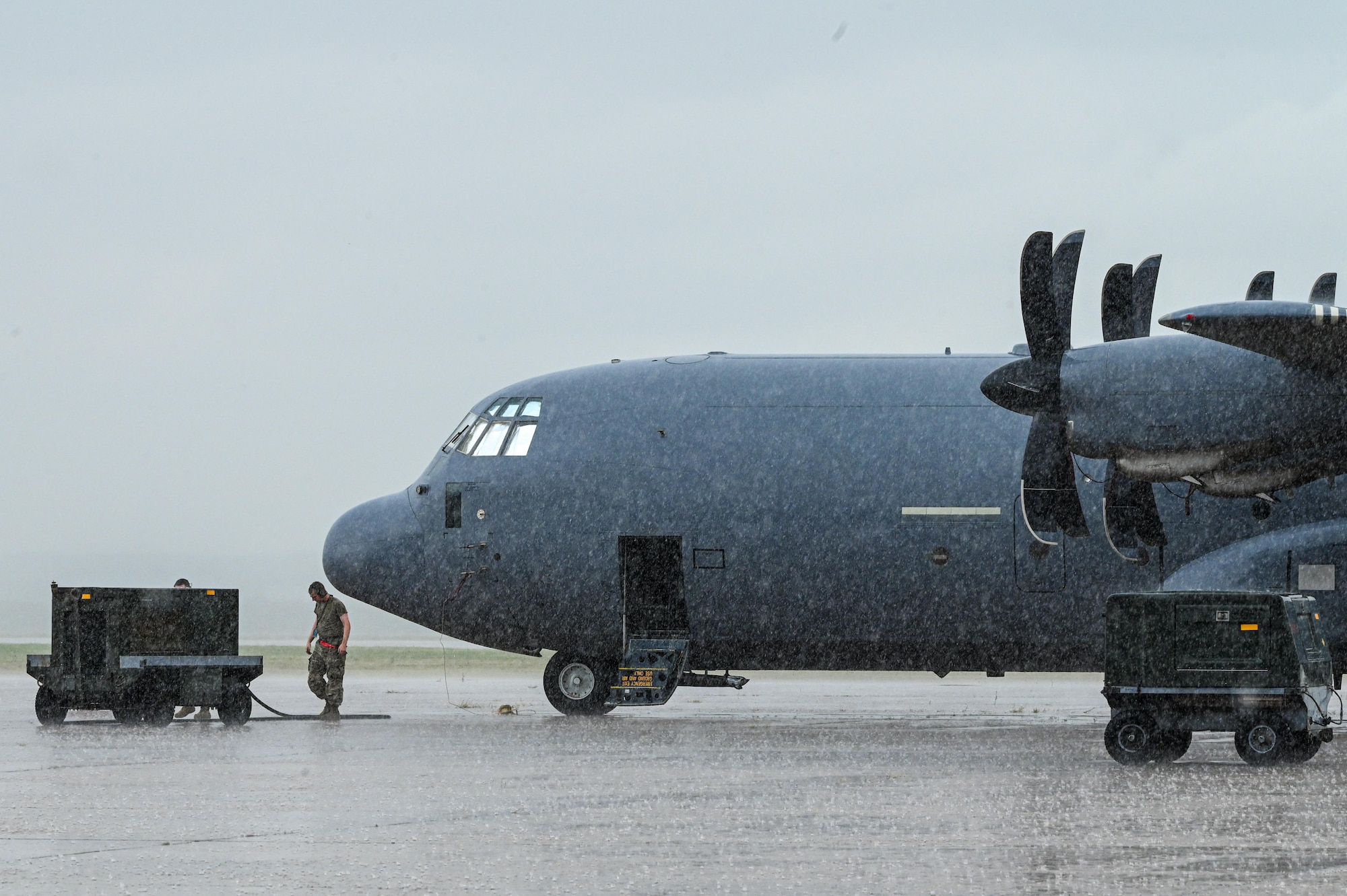 U.S. Air Force Airmen assigned to the 317th Aircraft Maintenance Squadron prepare to connect a power cart to a C-130J Super Hercules in rain during a Combat Readiness Inspection at Dyess Air Force Base, Texas, July 1, 2025. Despite adverse weather, Airmen executed rapid deployment tasks to validate the wing’s ability to generate and employ combat-ready airpower. (U.S. Air Force photo by Airman 1st Class Adrien Tran)