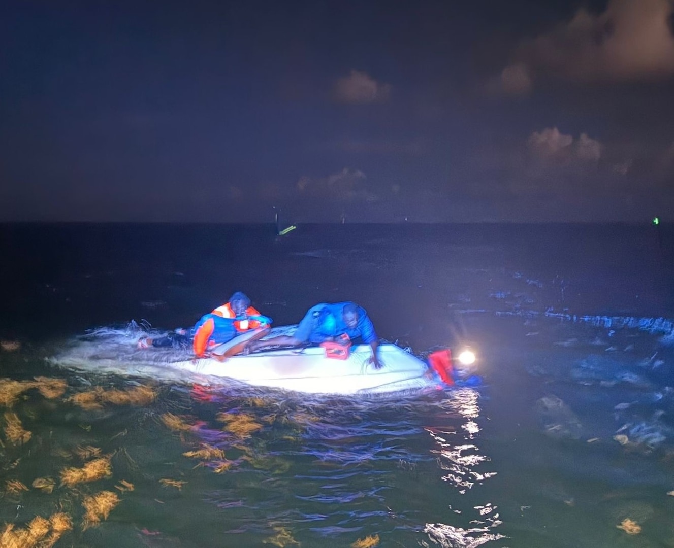 Three men cling to a capsized vessel