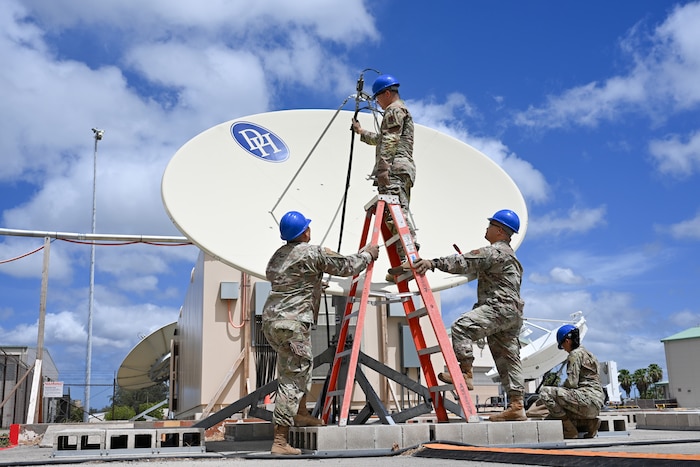 Four Airmen from the 109th Electromagnetic Warfare Squadron work on equipment. One Airman stands on a ladder while three others stand below, assisting with tuning a receiver.