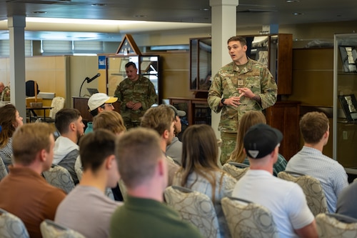 a tall handsome man in Air Force camouflage speaks to a crowd of people who are seated.