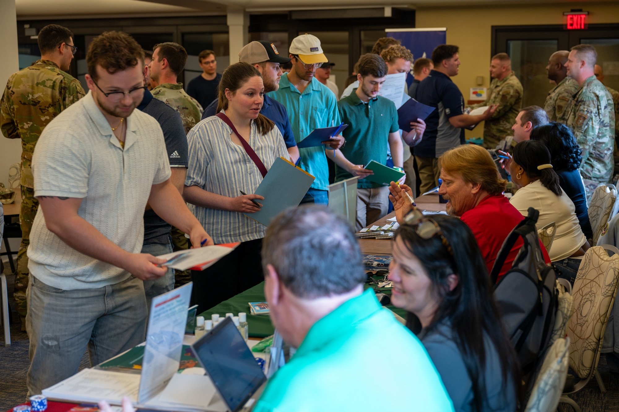 several people in civilian clothes stand in line. Other people behind tables and computers record their information.