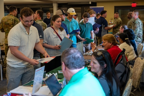 several people in civilian clothes stand in line. Other people behind tables and computers record their information.