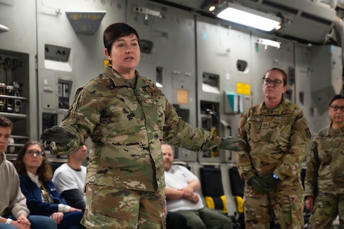 a woman in camouflage speaks to civilians on an air craft