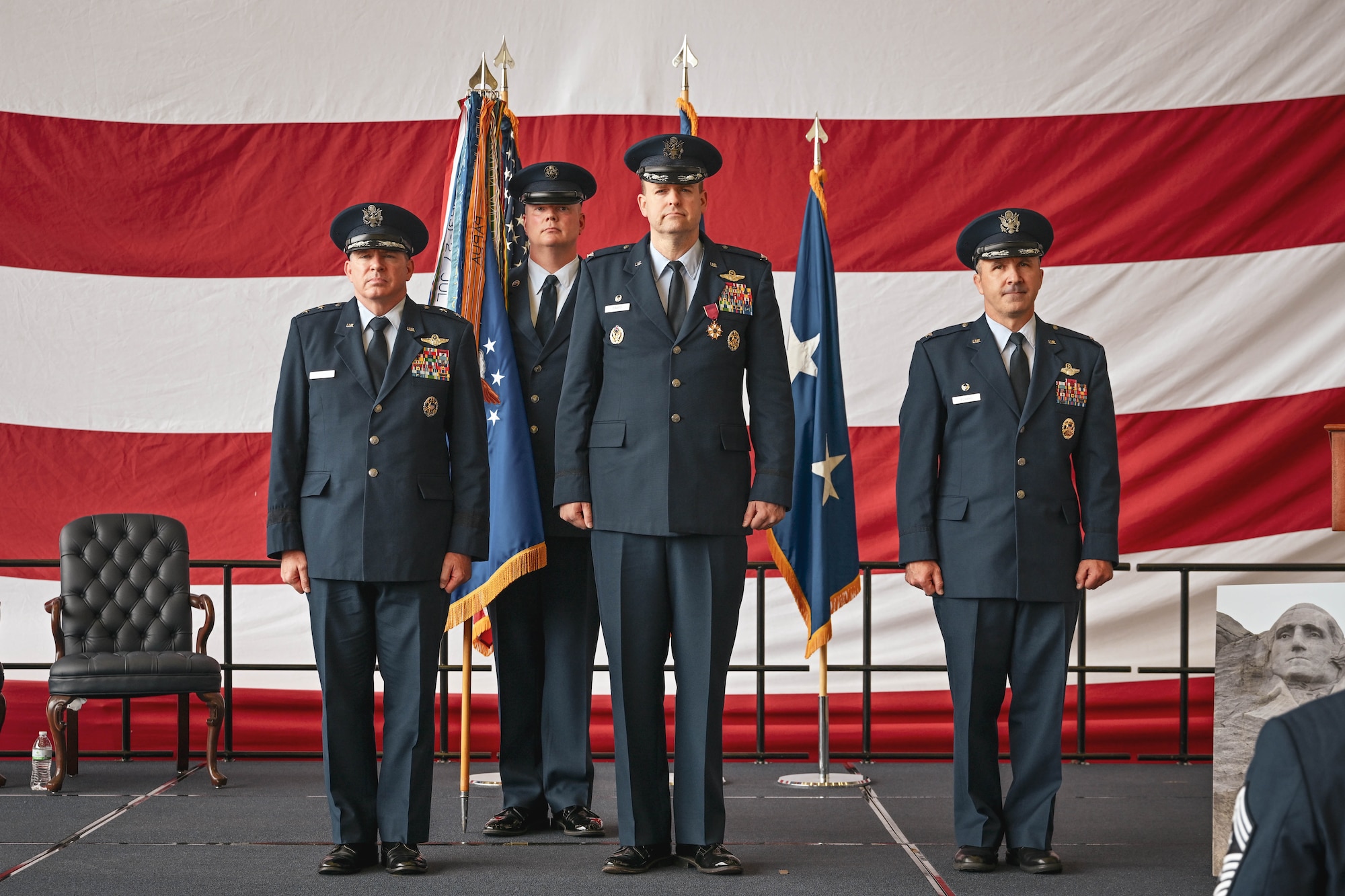Three military members stand on stage during a change of command ceremony.