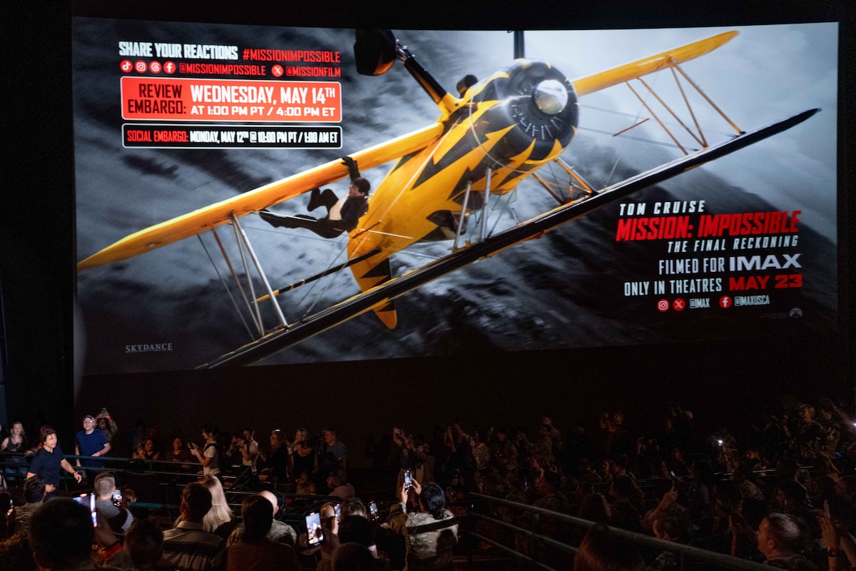 In a crowded movie theatre, actor Tom Cruise walks in front of a screen.