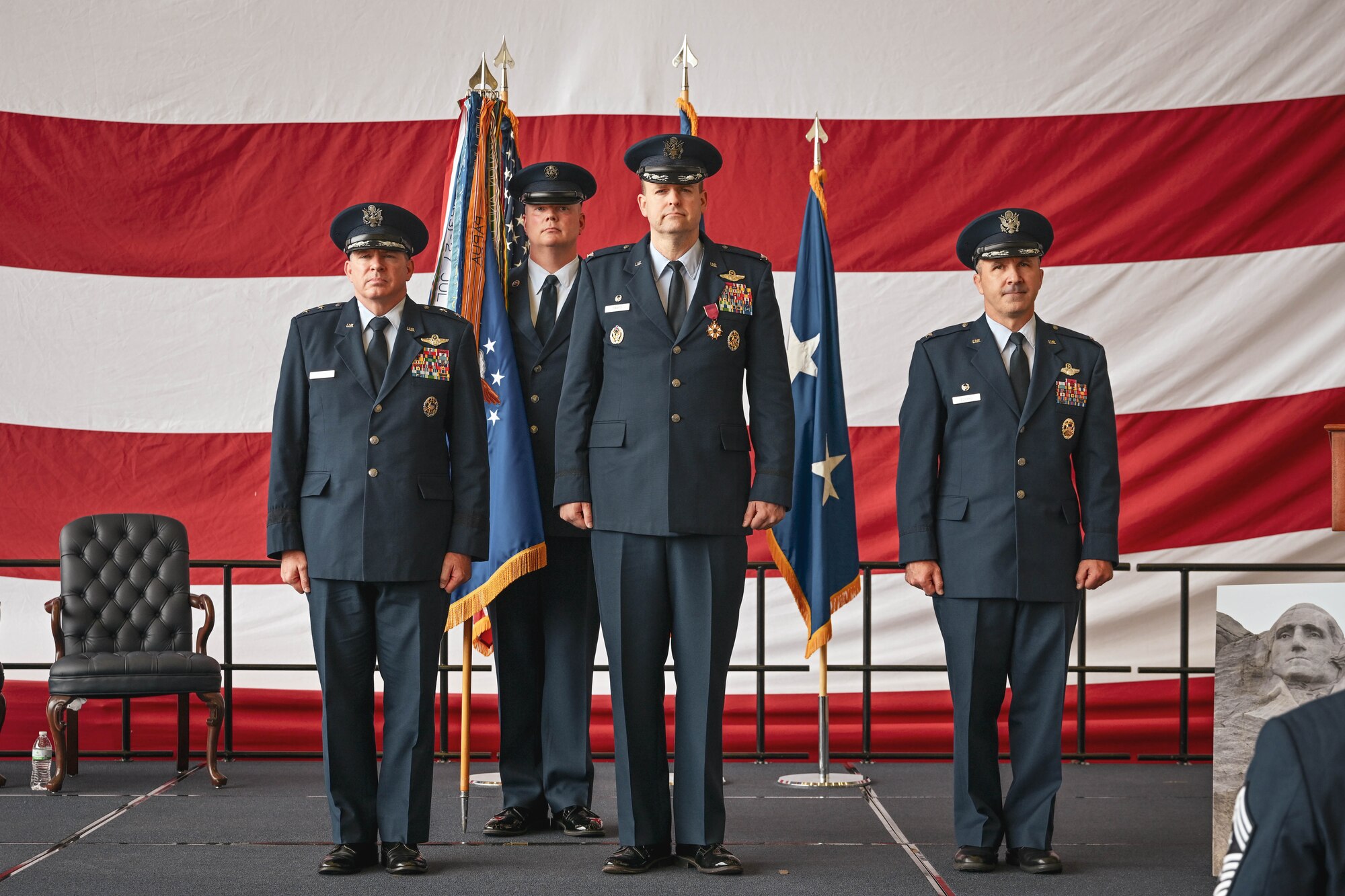 Three military members stand on stage during a change of command ceremony.