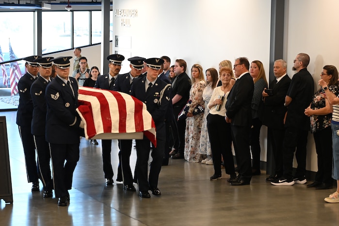 Honor guard members carry a casket holding the remains of Lt. Wilson into the museum in front of family members.