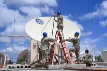 Four Airmen from the 109th Electromagnetic Warfare Squadron work on equipment. One Airman stands on a ladder while three others stand below, assisting with tuning a receiver.