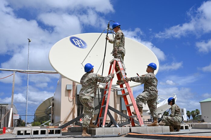 Four Airmen from the 109th Electromagnetic Warfare Squadron work on equipment. One Airman stands on a ladder while three others stand below, assisting with tuning a receiver.
