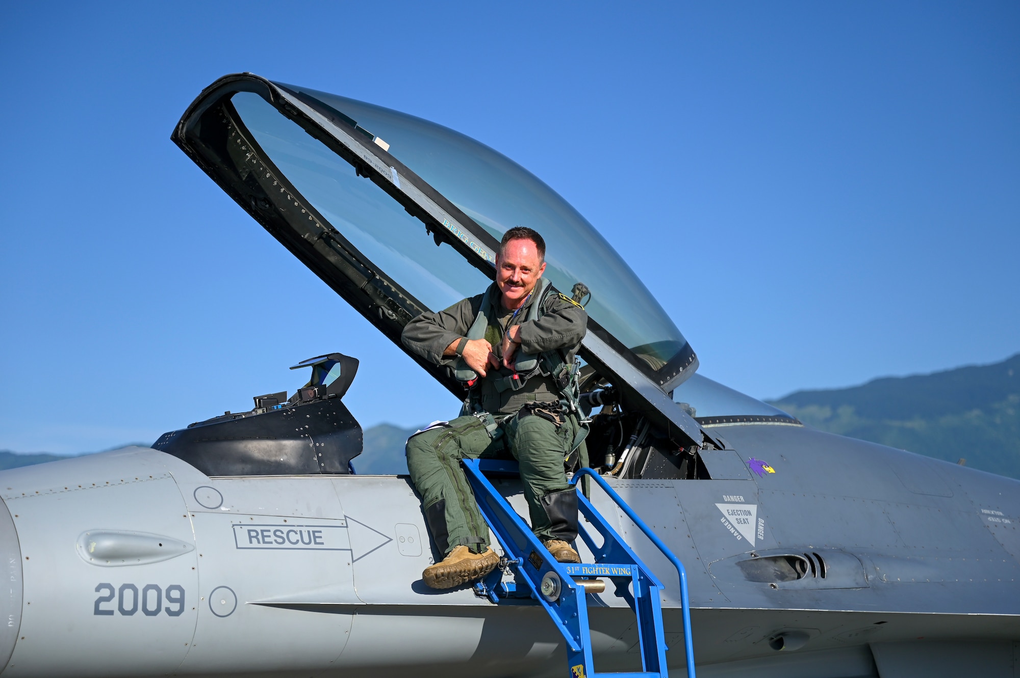Gen. Clark sits on a F-16 and smiles.