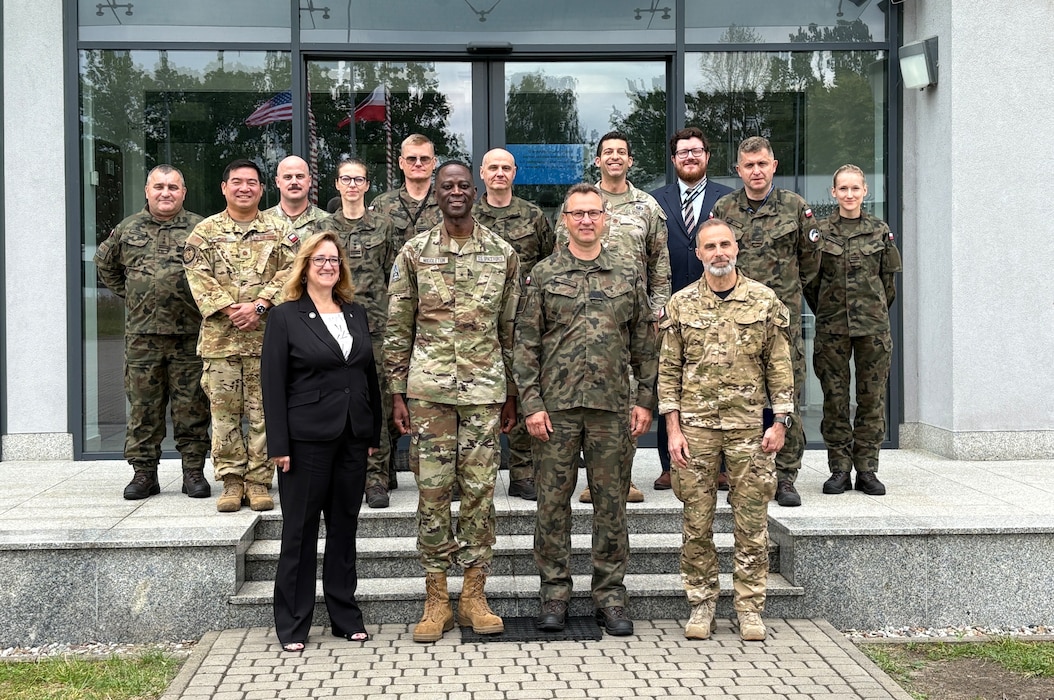 Two rows of U.S. and Polish officials stand on the steps in front of the entrance to a stark government building