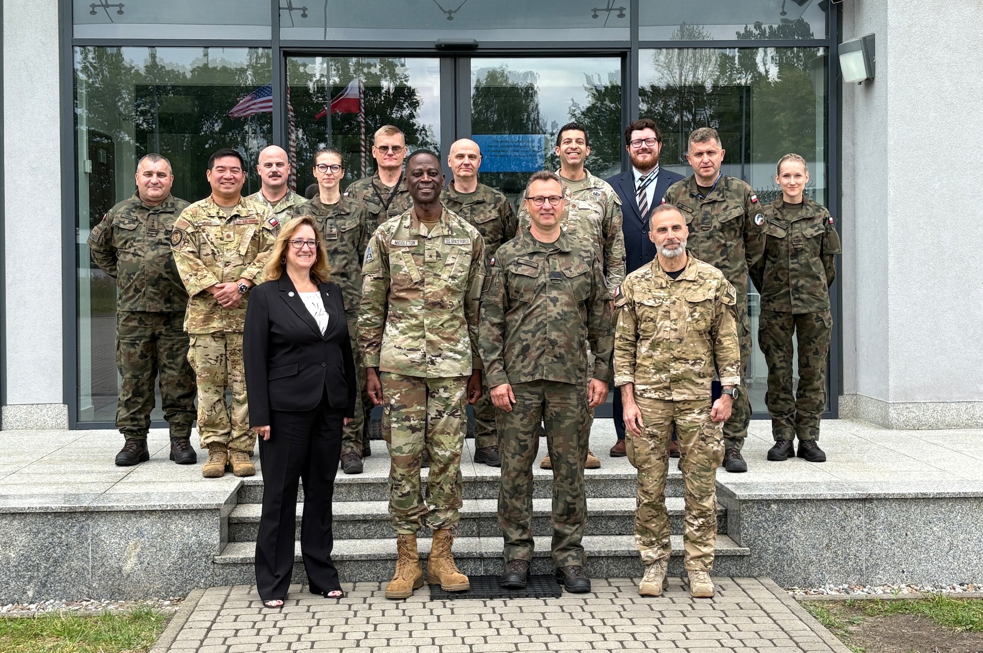 Two rows of U.S. and Polish officials stand on the steps in front of the entrance to a stark government building
