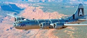 A large silver bomber with 2 engines on each wing flying in the sky