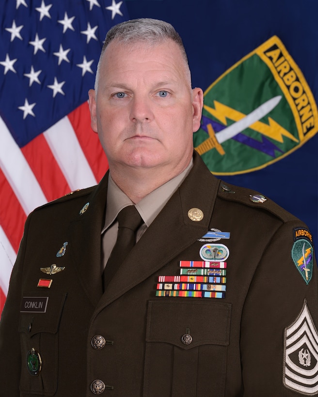 Photo of Command Sergeant Major George H. Conklin in front of the  U.S. Army Civil Affairs and Psychological Operations Command (ABN) and American flags